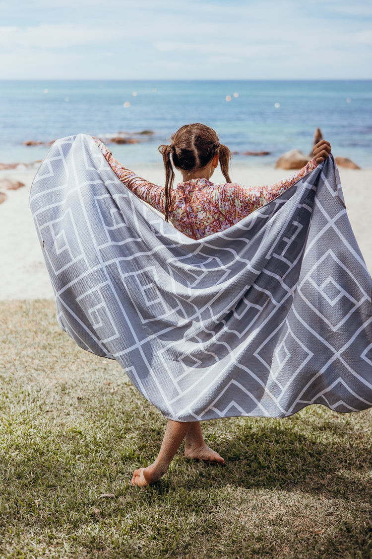 Girl holding up a grey Newlyfe waffle-weave towel on a grassy beach